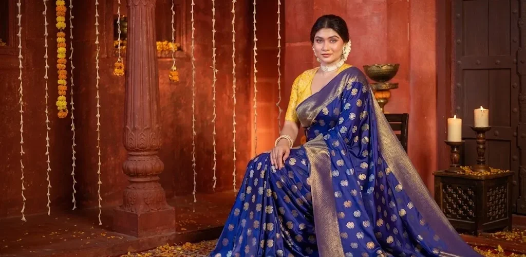 A woman wearing a royal blue Banarasi silk saree with golden motifs and traditional jewellery in a festive heritage-style setting