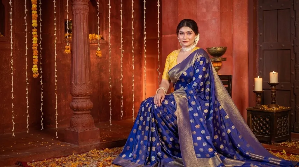 A woman wearing a royal blue Banarasi silk saree with golden motifs and traditional jewellery in a festive heritage-style setting