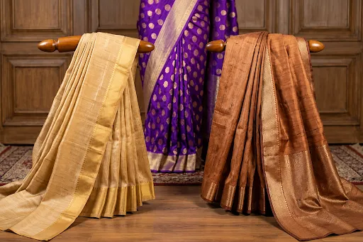 Collection of Banarasi silk sarees in purple, golden, and brown shades displayed on chairs showcasing traditional weaving and craftsmanship