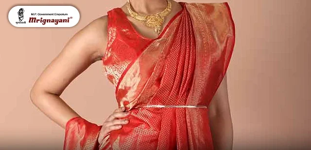 Woman wearing a traditional red silk saree with a stylish waist belt and gold jewellery.