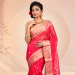 Indian woman wearing a vibrant pink silk saree with a golden zari border, styled with traditional gold jewellery for a festive ethnic look.