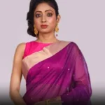 Indian woman modelling a rich purple Chanderi saree with a sleeveless pink blouse and gold dangling earrings.