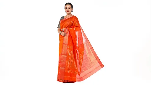 Indian woman wearing a vibrant orange-red silk saree featuring delicate golden woven motifs, a decorative border and a flowing pallu.